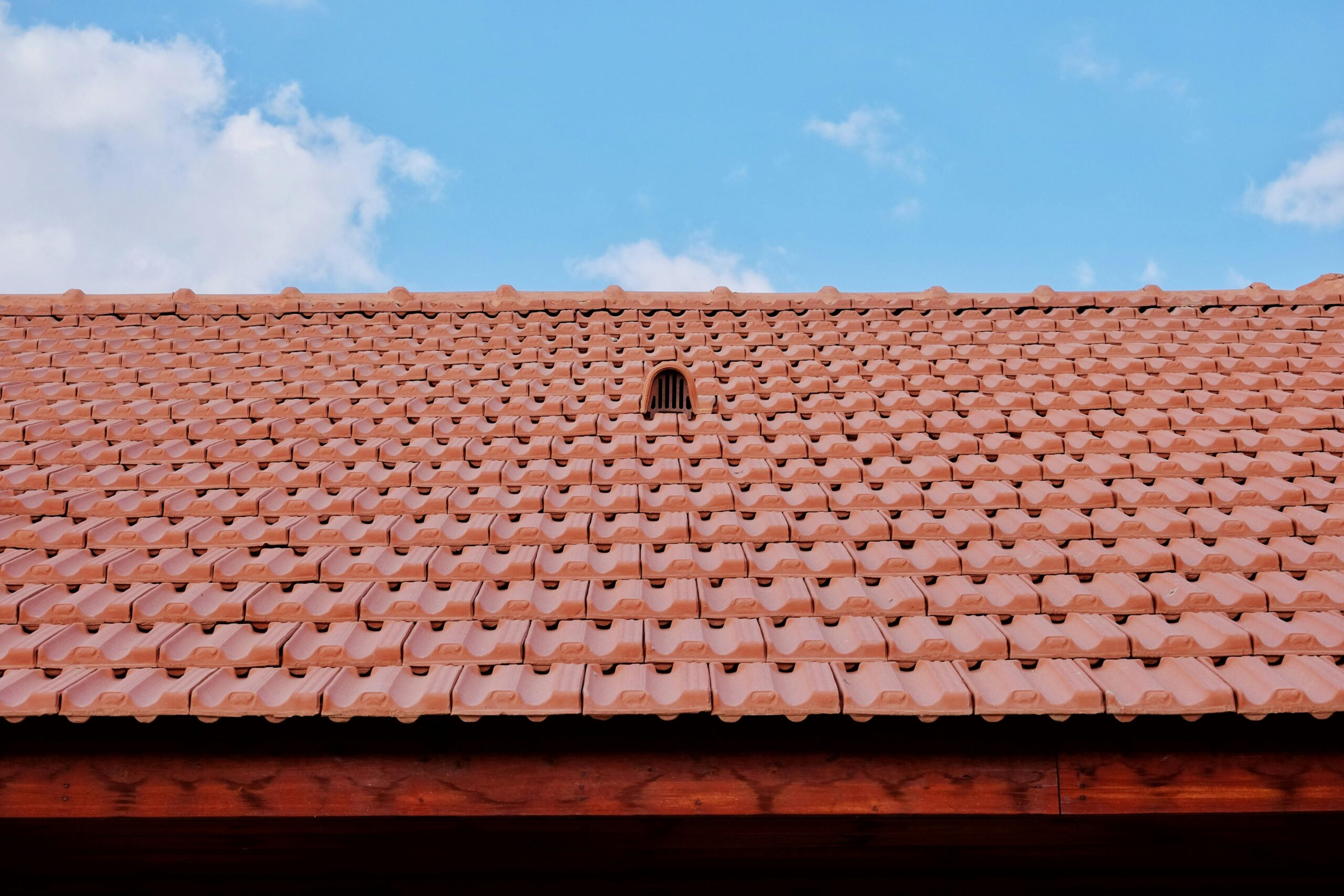 Roofing Services Los Angeles | Safeguard A detailed view of a red tiled roof with vent against a clear blue sky, showcasing architectural design.